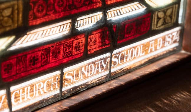 Stained glass detail with intricate red and white designs that reads 'Trinity Church Sunday School AD 1874'