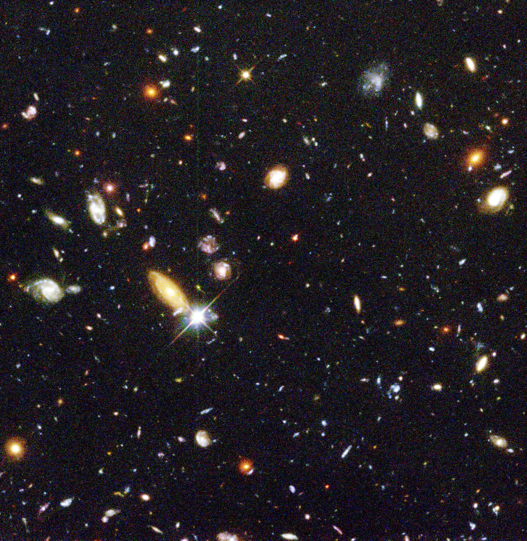 image from the Hubble telescope showing many distant galaxies, colored orange, pale blue, and white, in the dark night sky. Image via NASA/JPL